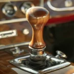 A vintage car's stick shift with a wooden handle and chrome accents, surrounded by aged leather upholstery and classic dials, captured in warm golden-hour sunlight. The image symbolizes downshifting as a mindful practice in both driving and life, reflecting balance, intentionality, and timeless wisdom.